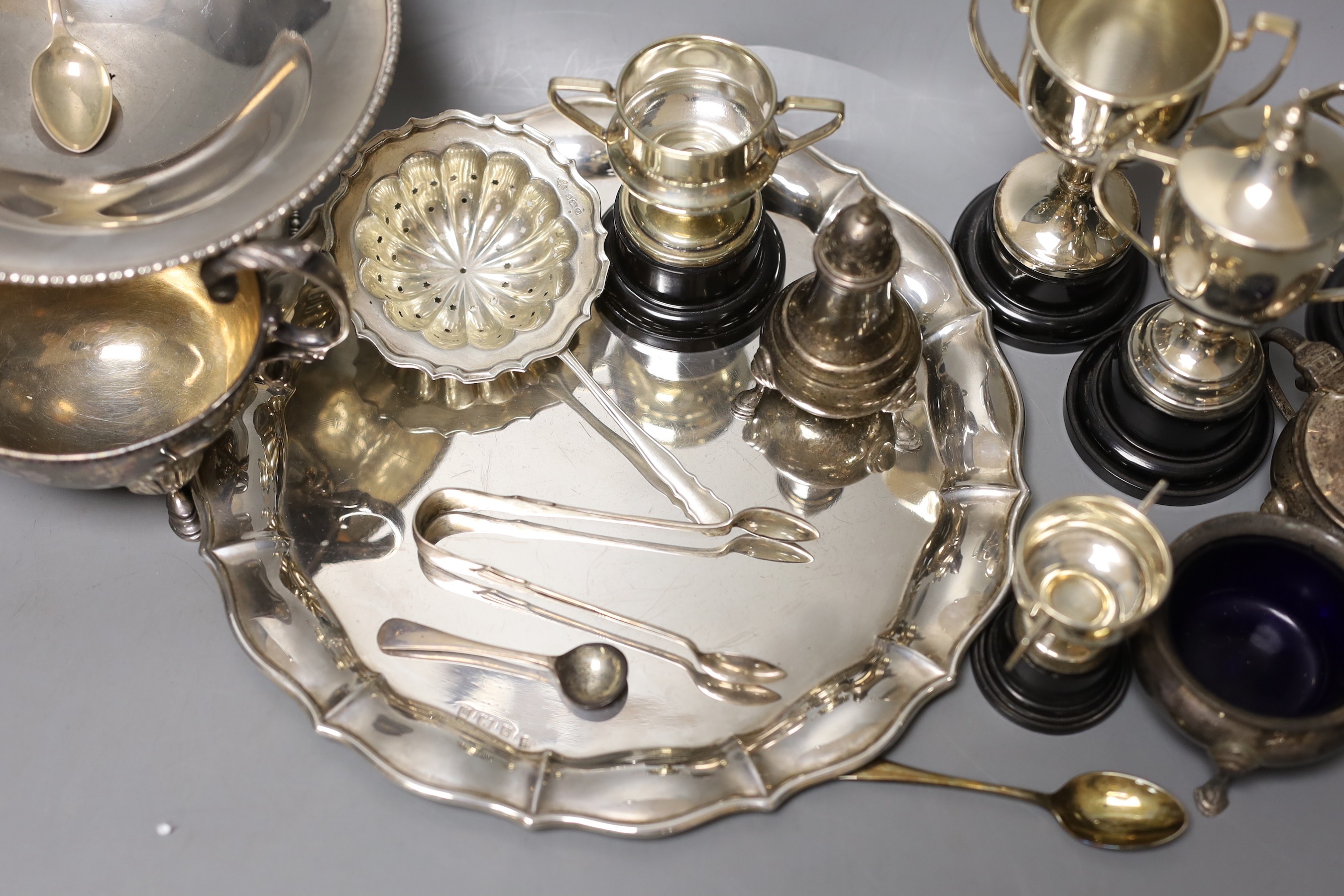 A George V silver salver, a silver tazze, a silver sauceboat, three silver condiments, a silver tea strainer, four items of silver flatware, three small silver trophy cups and two plated cups.